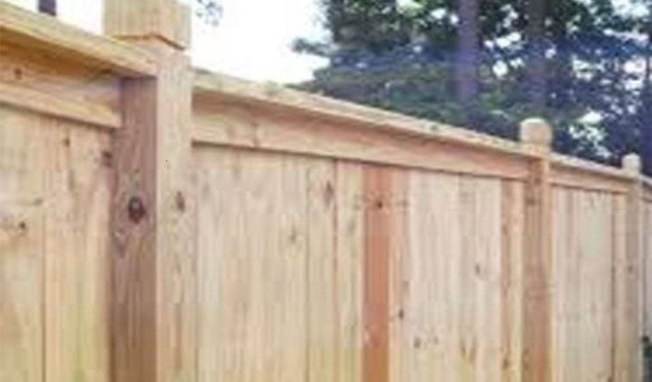 Wooden privacy fence made of vertical planks with horizontal support beams and post caps, set outdoors with trees in the background.